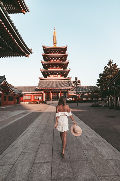 During the day, a woman in a white dress with a white umbrella walking in gray cement road
